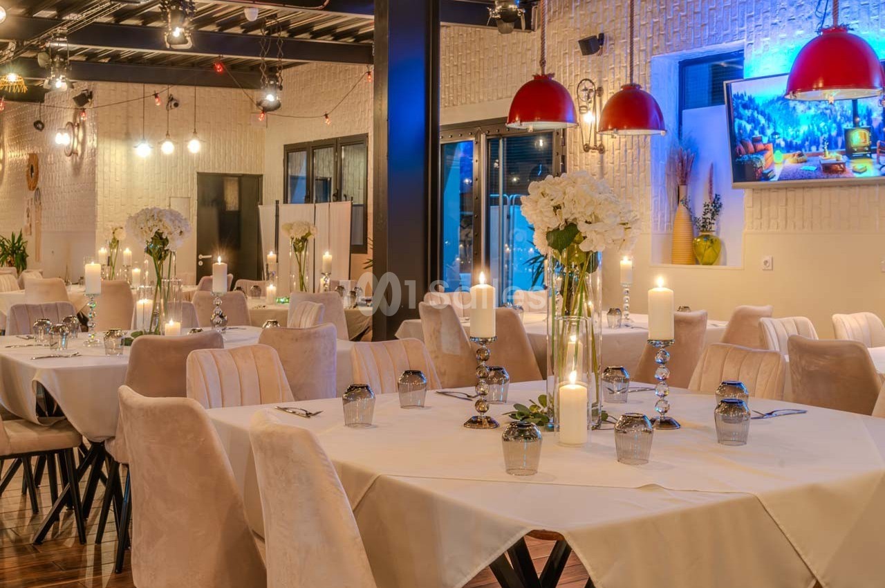 Salle de restaurant élégante avec tables dressées, chandeliers, fleurs blanches et éclairage chaleureux.
