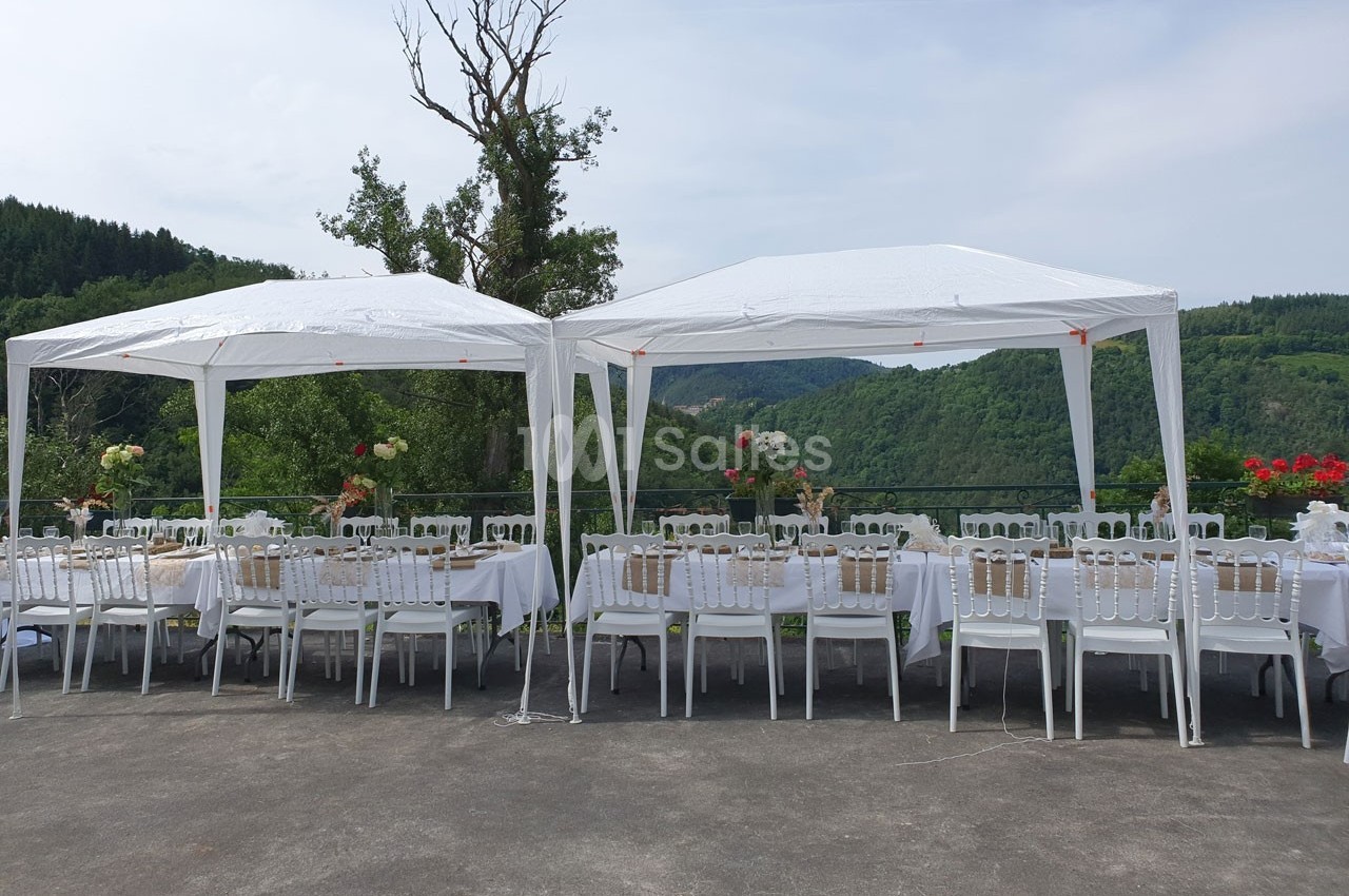 Deux tonnelles blanches abritent des tables dressées pour un repas en extérieur, avec vue sur un paysage vallonné.