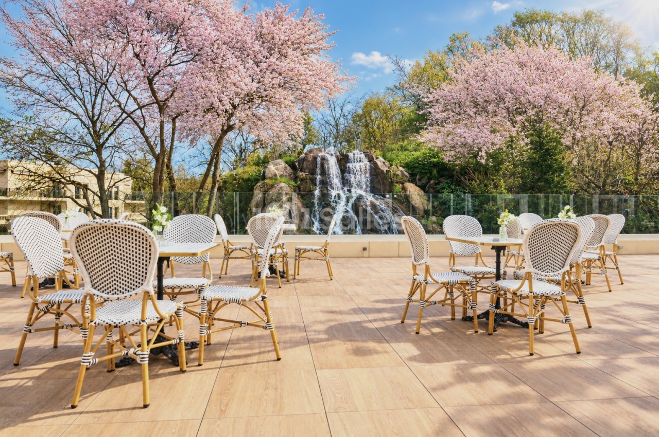 Terrasse ensoleillée avec chaises en rotin blanc et cascatelle, cerisiers en fleurs roses en arrière-plan.