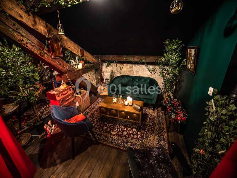 Salon cosy sous des poutres apparentes, décoré avec des plantes, un canapé vert et des bougies sur une table basse.