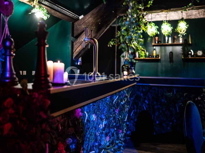Comptoir de bar décoré de feuillages et bougies, avec un robinet à bière, dans une ambiance tamisée et végétale.