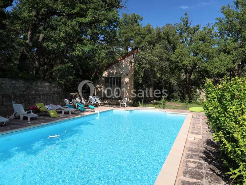 Piscine extérieure entourée de chaises longues, située près d'une maison en pierre et bordée d'arbres.