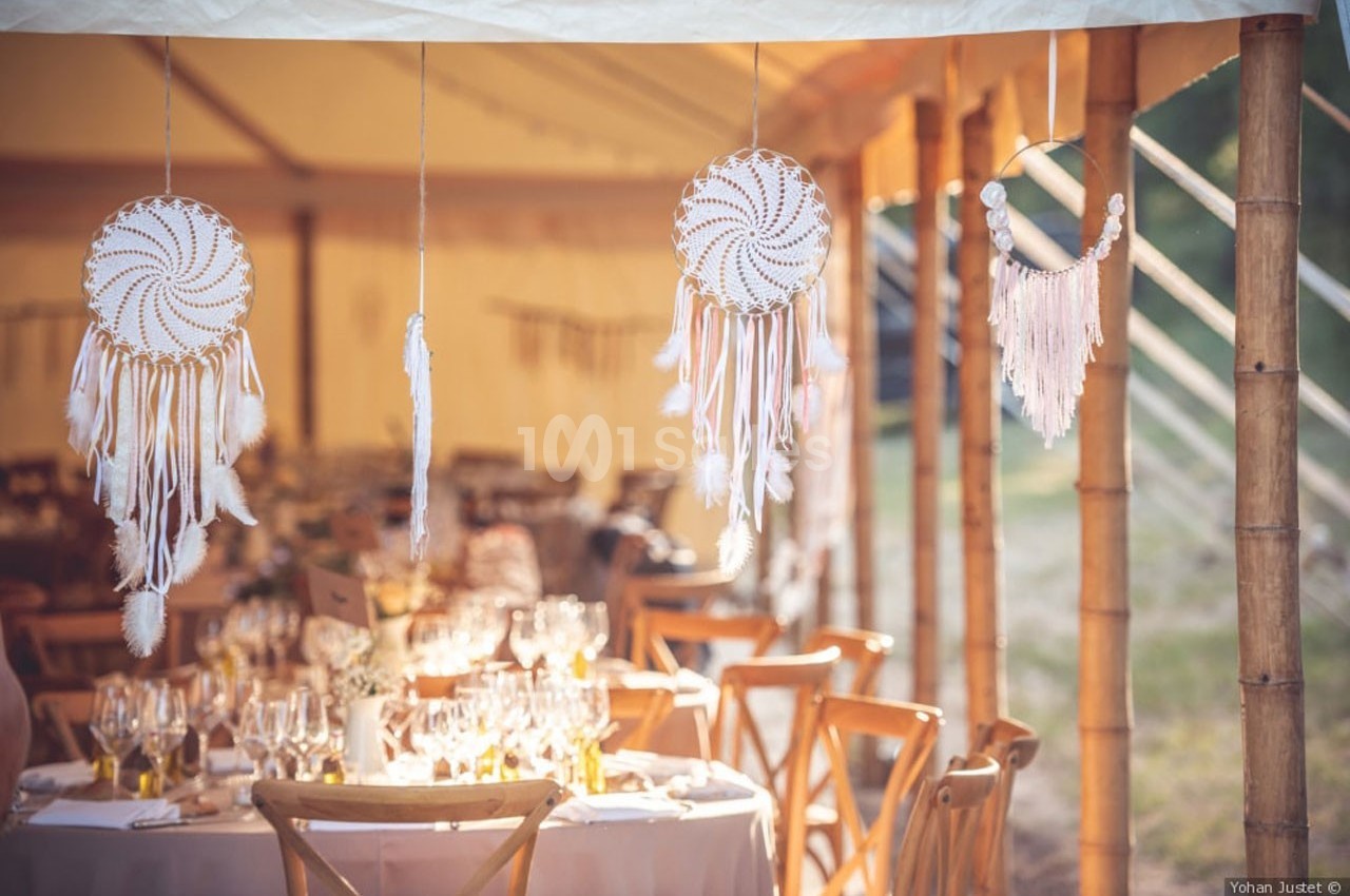 Décoration de mariage avec attrape-rêves suspendus et tables dressées sous une tente lumineuse en bambou.