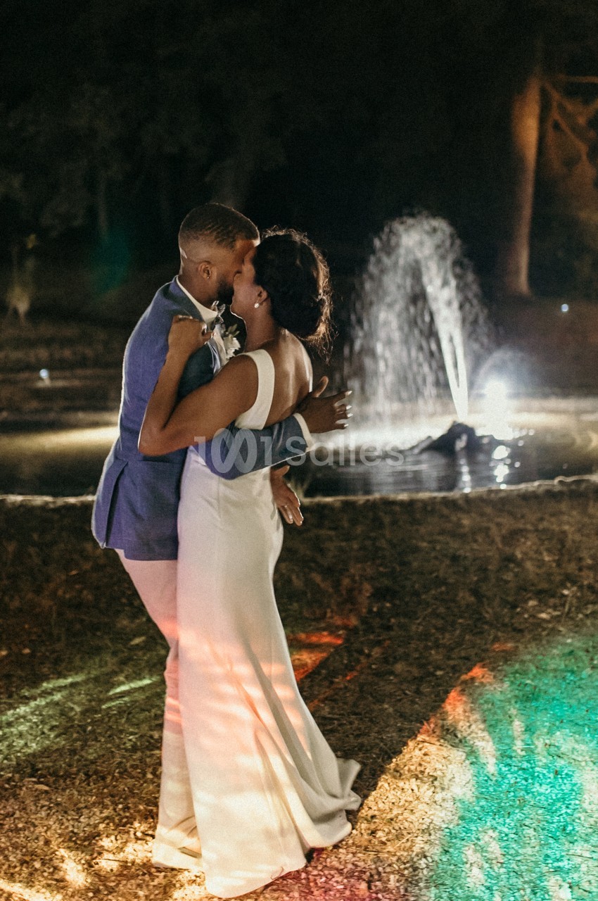 Un couple danse tendrement le soir près d'une fontaine illuminée dans un cadre extérieur.