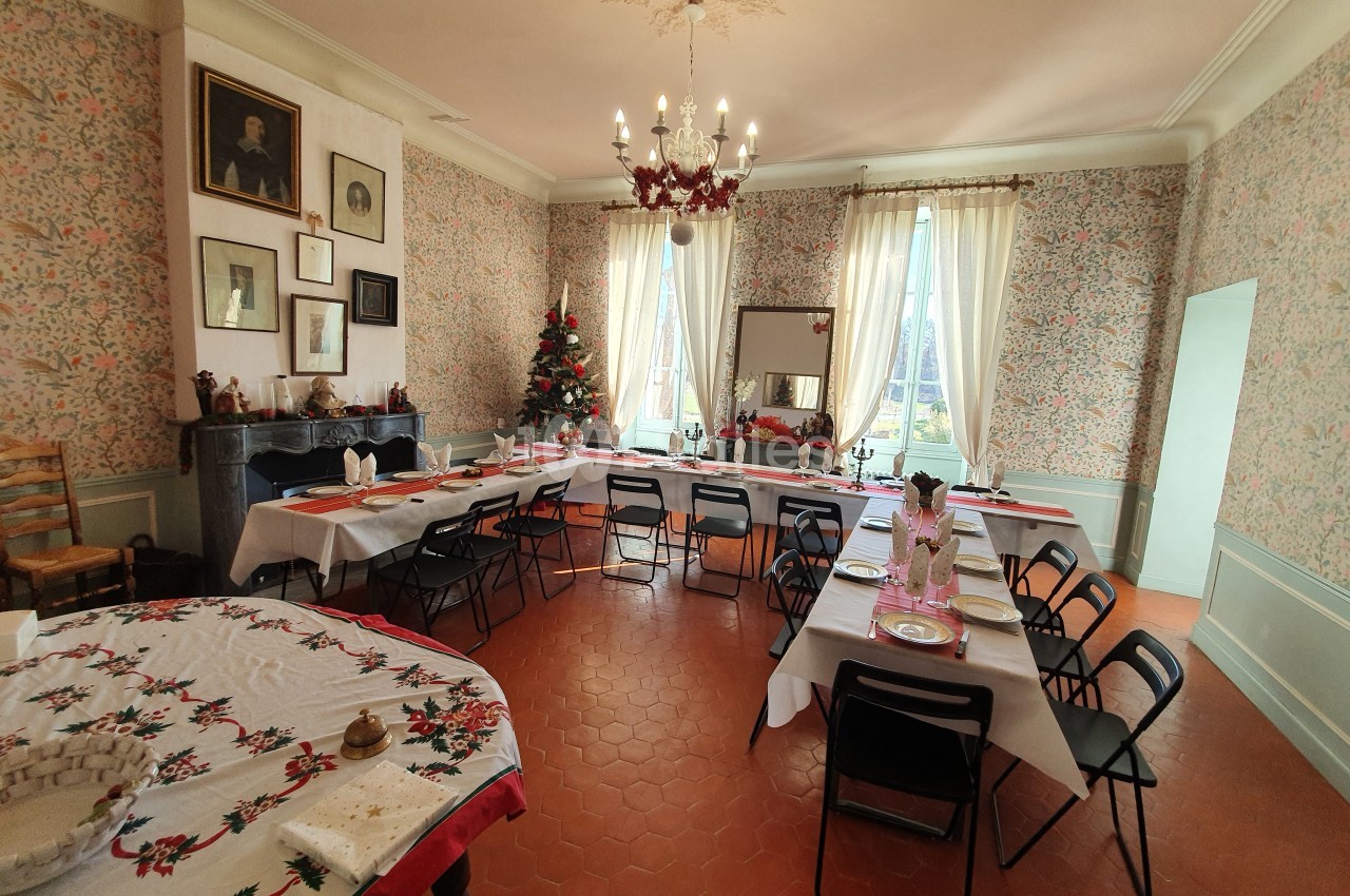 Salle à manger décorée pour Noël avec une grande table dressée, un sapin et des murs ornés de papier peint floral.