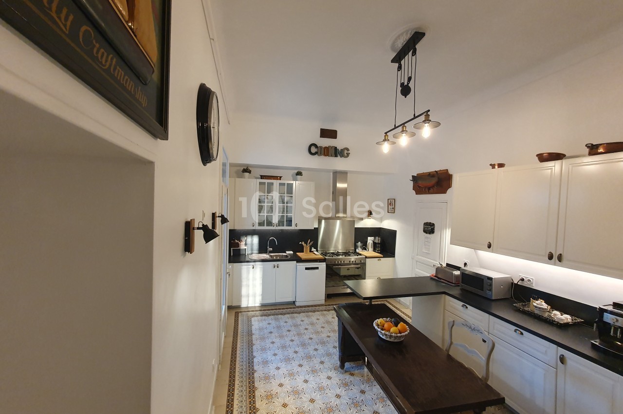 Cuisine lumineuse avec meubles blancs, plan de travail noir, table en bois, et sol à motifs décoratifs.