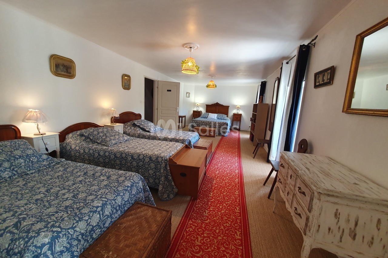Chambre spacieuse avec trois lits, tapis rouge central, murs blancs et mobilier en bois dans un style classique.