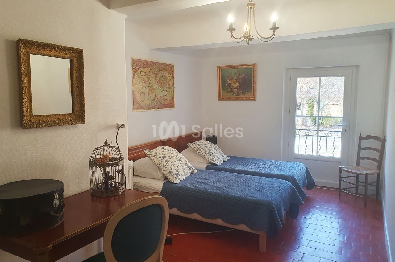 Chambre lumineuse avec deux lits simples, bureau en bois, décorations murales et fenêtre donnant sur l'extérieur.
