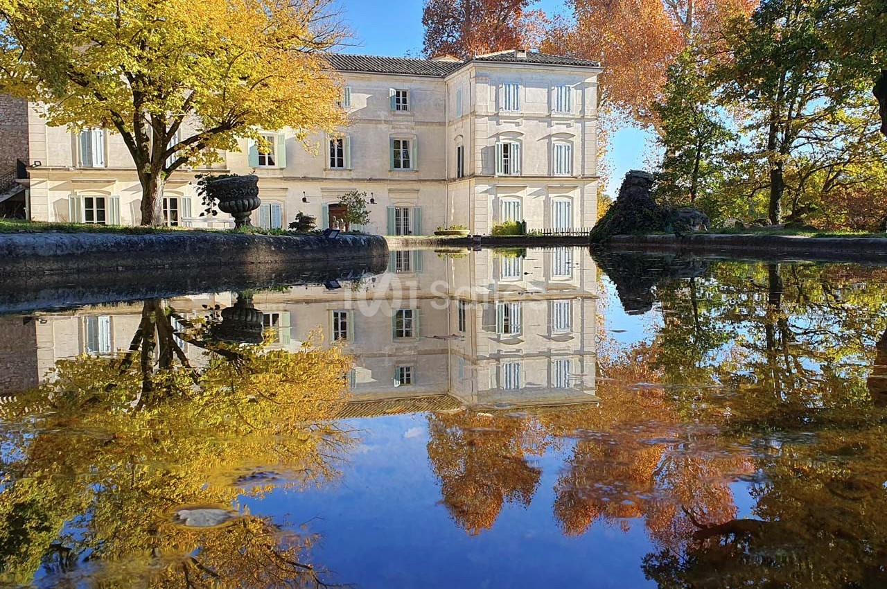 Reflet d'un bâtiment ancien entouré d'arbres aux couleurs automnales dans un plan d'eau calme.