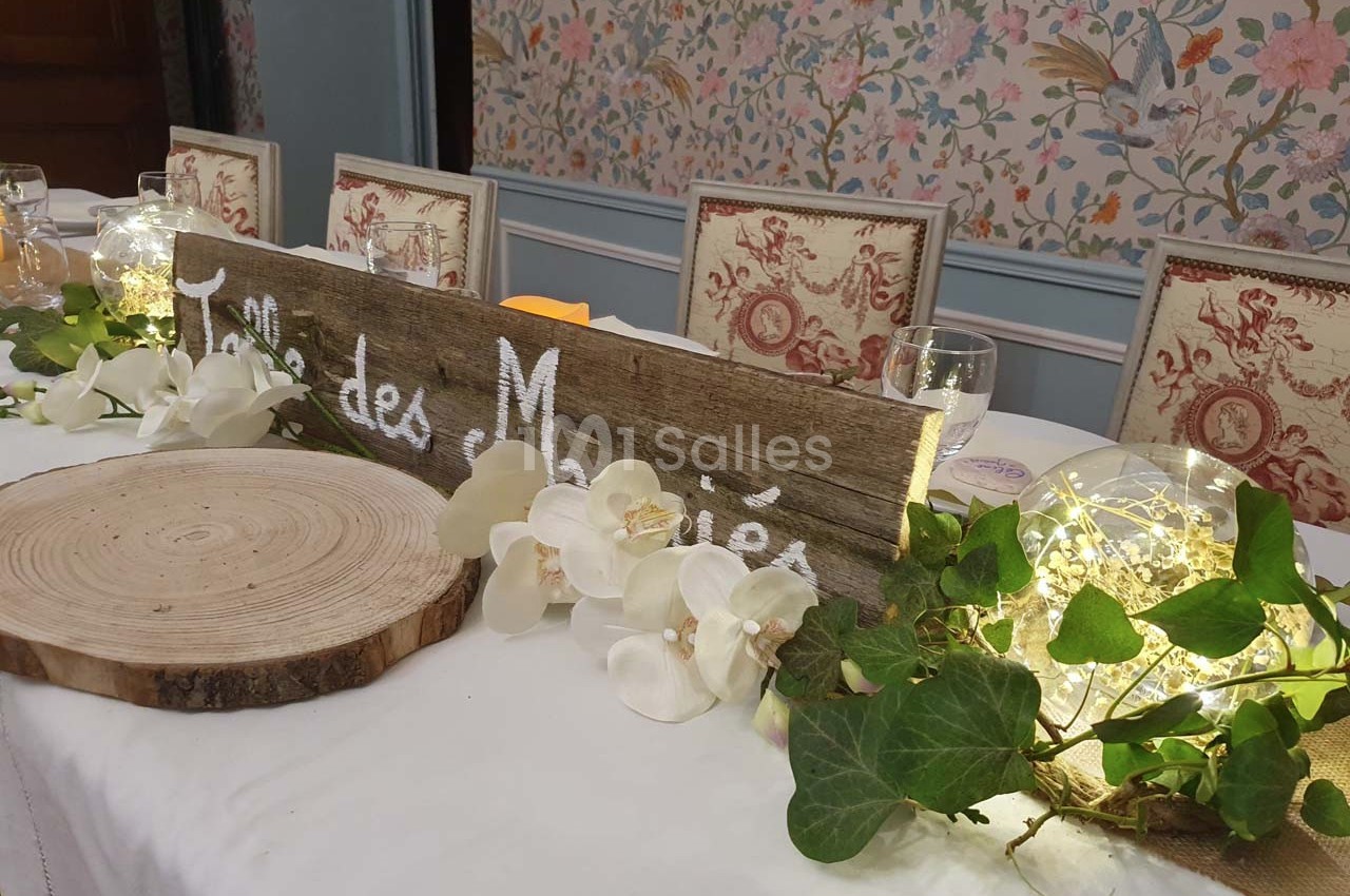 Table décorée pour un mariage avec une pancarte en bois, des orchidées blanches, du lierre et des guirlandes lumineuses.