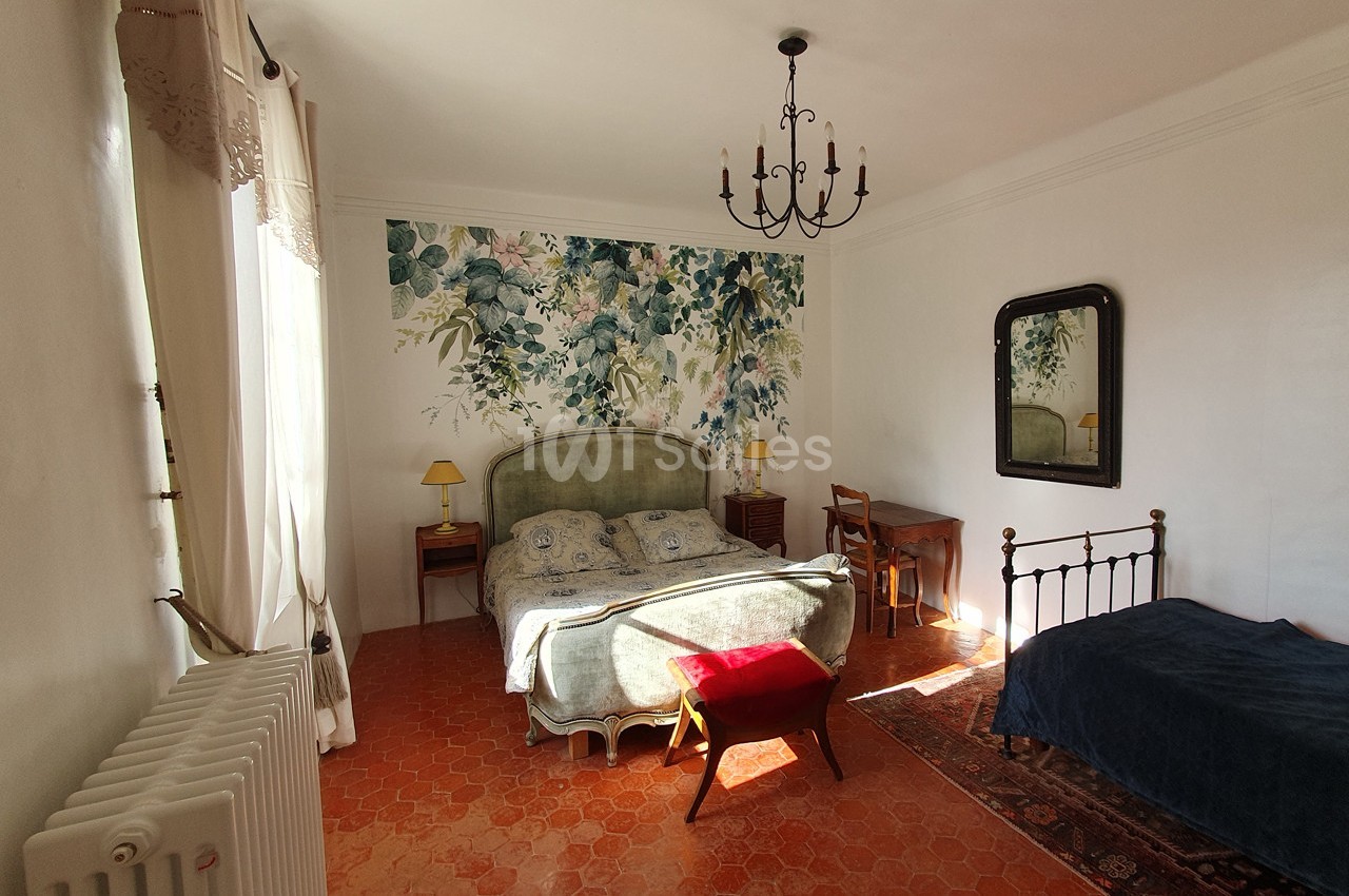 Chambre lumineuse avec un lit double, un lit simple, un bureau, un miroir et une décoration murale florale.