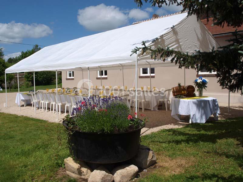 Tente blanche installée dans un jardin, abritant des tables dressées avec des nappes blanches et des chaises alignées.