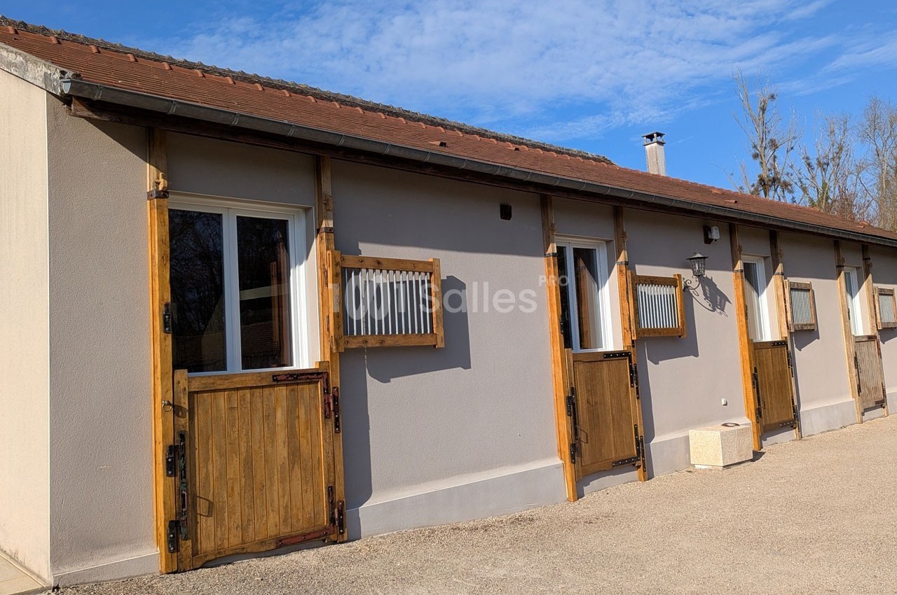 Façade d'un bâtiment avec des portes en bois et des fenêtres à volets, sous un ciel bleu dégagé.