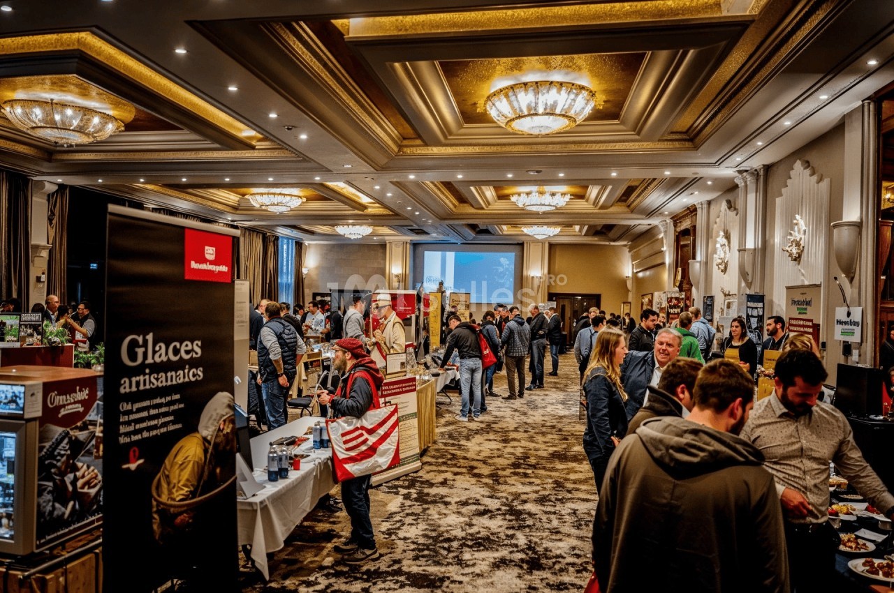 Des visiteurs échangent et découvrent des stands dans une salle d'exposition lumineuse au décor élégant.