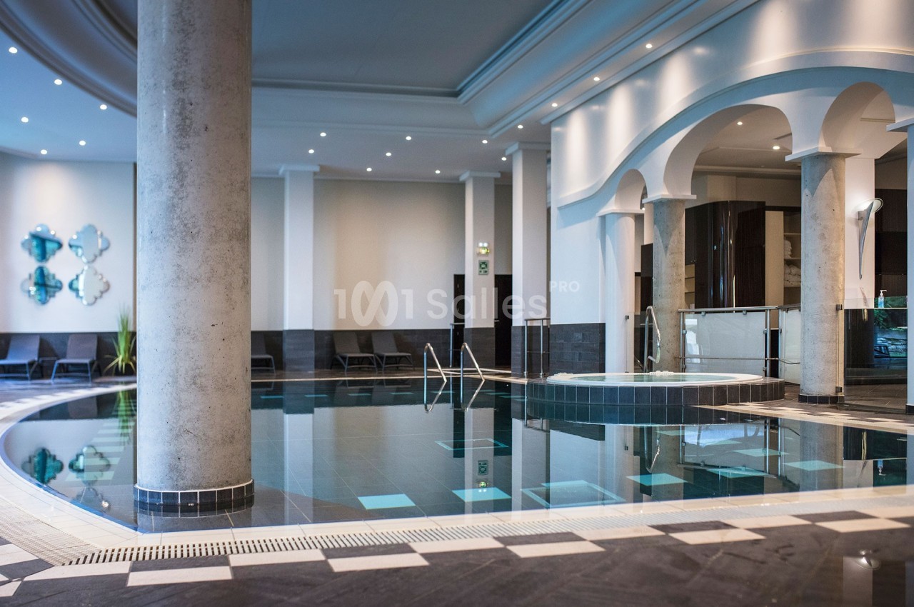 Piscine intérieure moderne avec colonnes, chaises longues et éclairage tamisé dans un espace élégant.