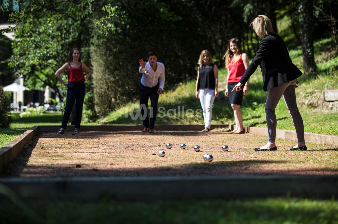 Des personnes jouent à la pétanque sur un terrain en plein air, entouré de verdure.