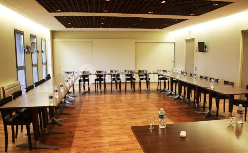 Salle de réunion lumineuse avec tables disposées en U, chaises noires et bouteilles d'eau sur les tables.