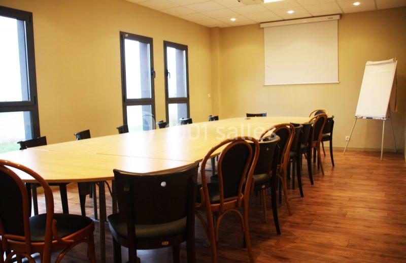 Salle de réunion avec une grande table en bois entourée de chaises, un tableau blanc et un écran de projection.