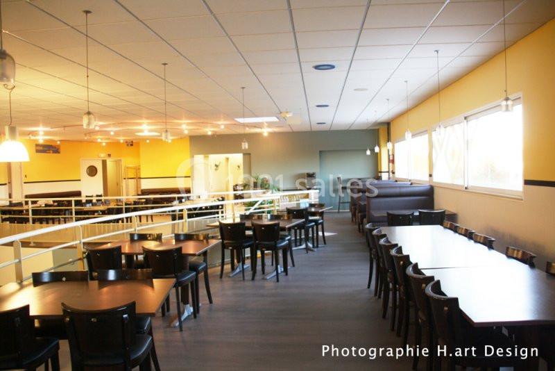 Salle de restaurant lumineuse avec tables en bois foncé, chaises noires et fenêtres laissant entrer la lumière naturelle.