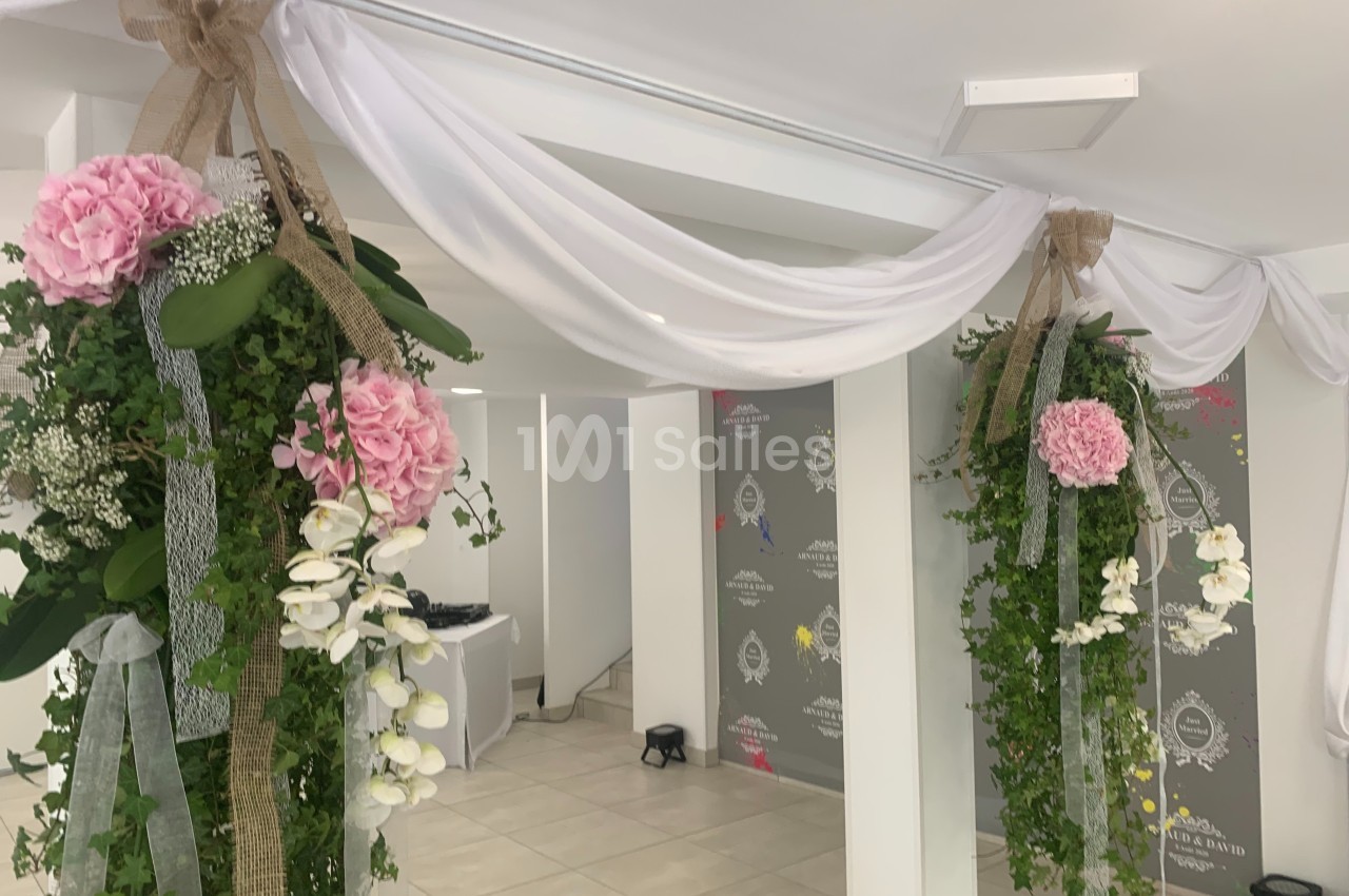 Décoration florale suspendue avec des drapés blancs, des fleurs roses et blanches, et du feuillage dans une salle lumineuse.