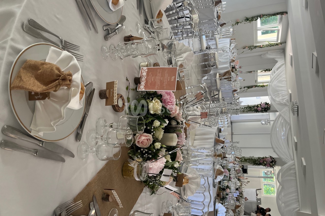 Table de réception élégamment dressée avec nappes blanches, vaisselle raffinée, centre de table floral et décoration…