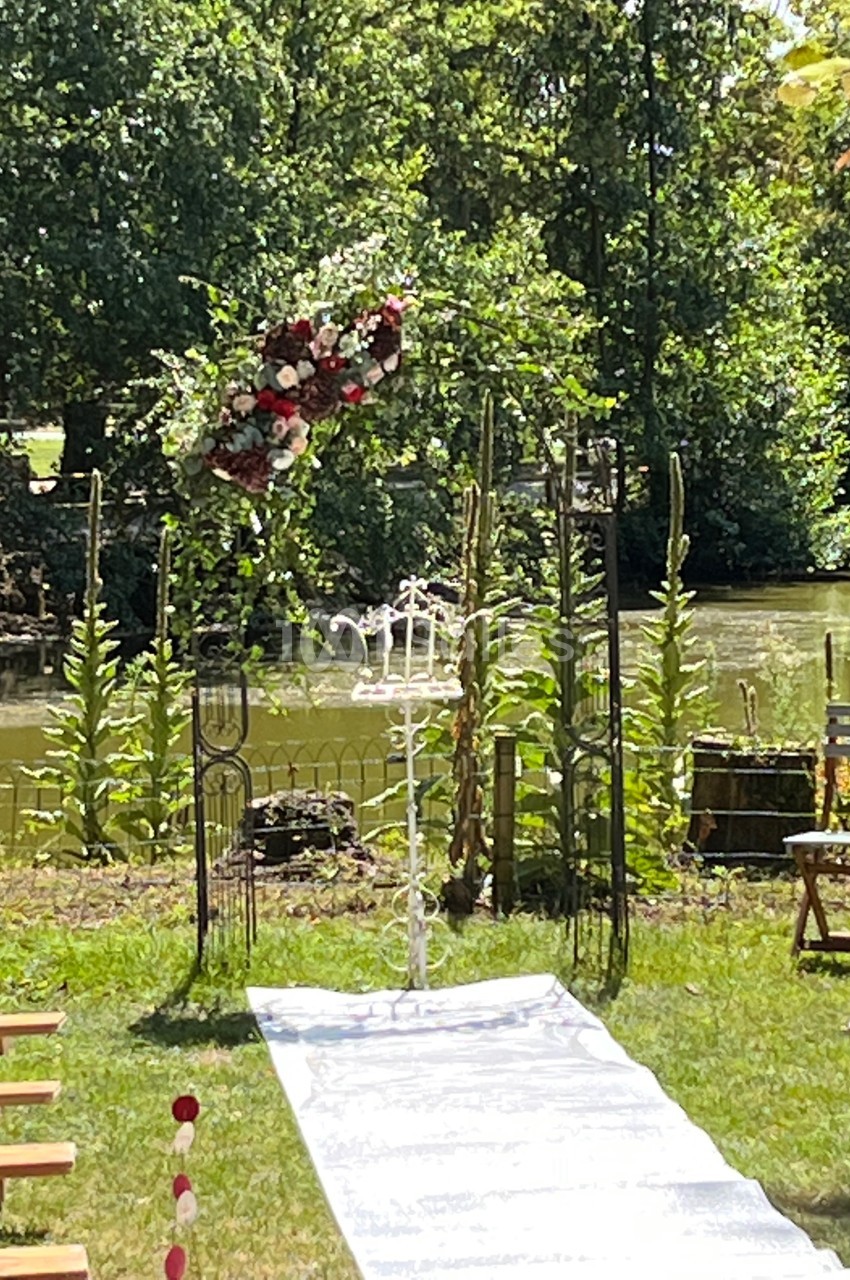 Arche fleurie et allée blanche installées en extérieur près d'une rivière pour une cérémonie.