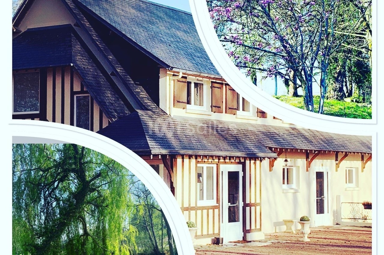 Maison à colombages avec toit en ardoise, entourée d'arbres fleuris et d'un grand jardin verdoyant.