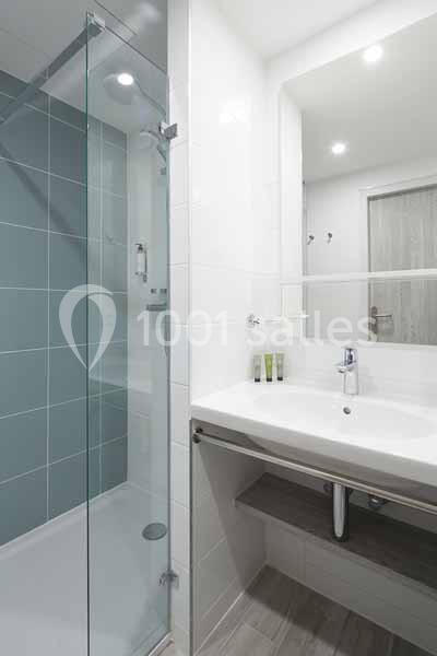 Salle de bain moderne avec douche à paroi vitrée, lavabo blanc et grand miroir éclairé.