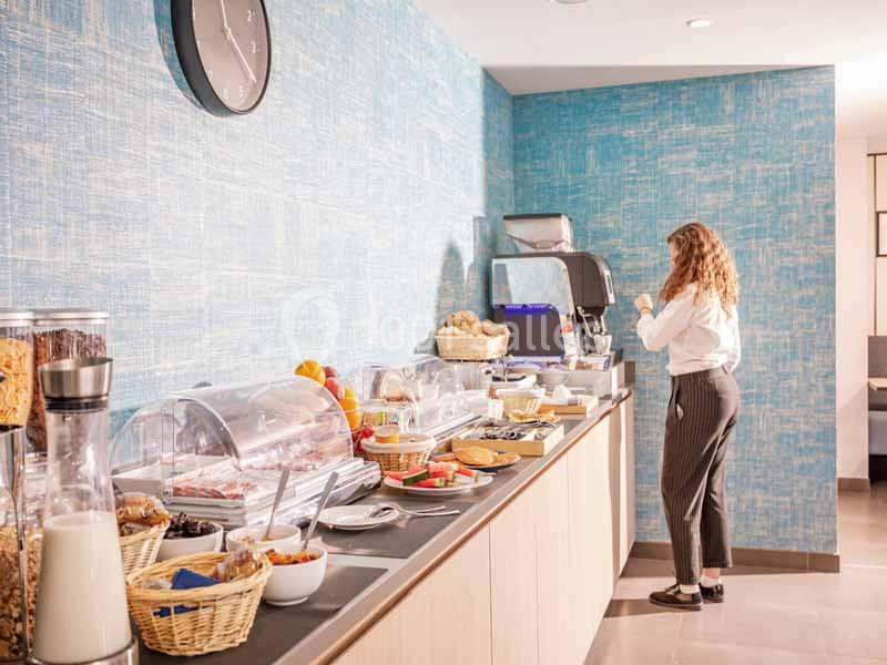 Une femme se sert une boisson chaude dans un buffet de petit-déjeuner avec divers aliments disposés sur un comptoir.