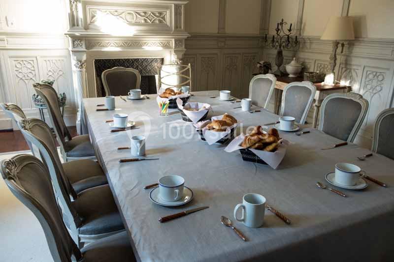 Table dressée pour un petit-déjeuner avec croissants, tasses, couteaux et cuillères dans une salle élégante.
