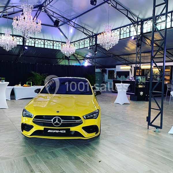 Voiture jaune Mercedes-AMG exposée dans une salle élégante avec lustres et tables hautes en arrière-plan.