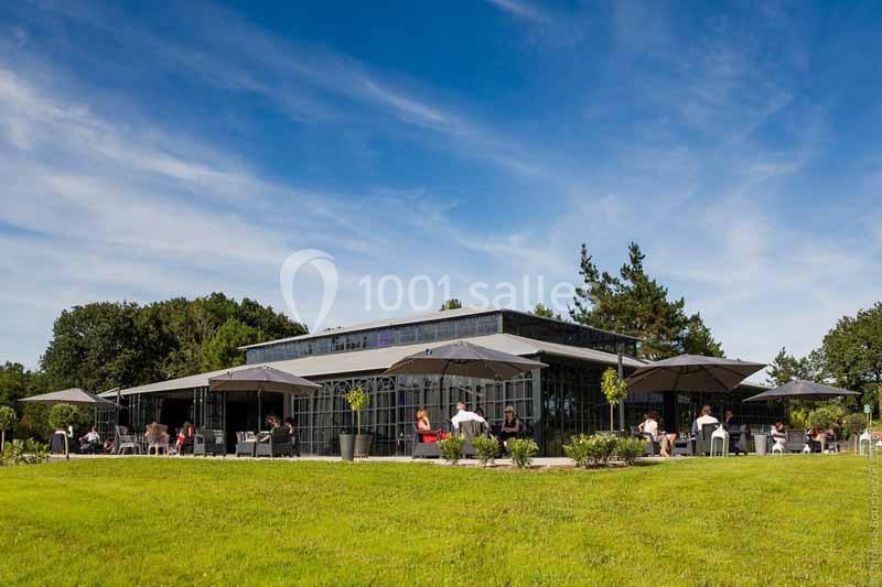 Terrasse d'un restaurant moderne avec parasols, entourée de verdure sous un ciel bleu dégagé.