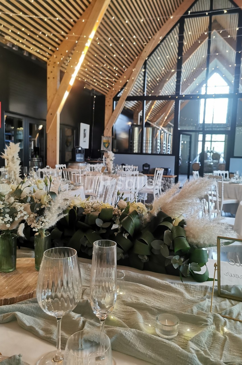 Salle de réception décorée avec des tables élégantes, des fleurs blanches et des éléments naturels sous une charpente en…
