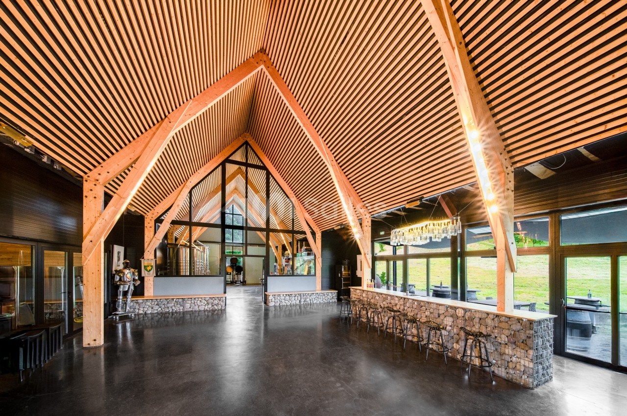 Intérieur d'un bâtiment moderne avec une charpente en bois apparente, des murs vitrés et un comptoir en pierre.