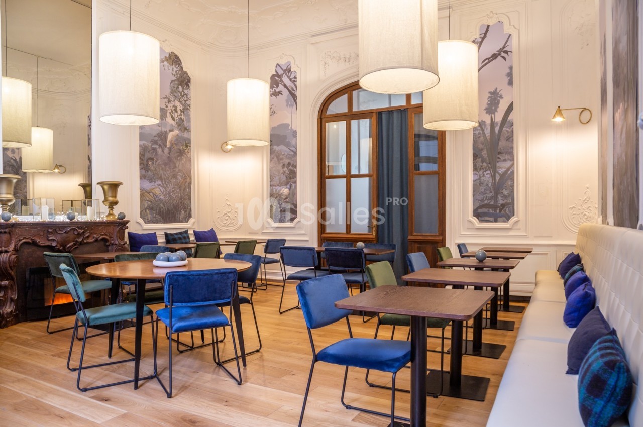 Salle lumineuse avec tables en bois, chaises bleues, banquette blanche et décor mural élégant.