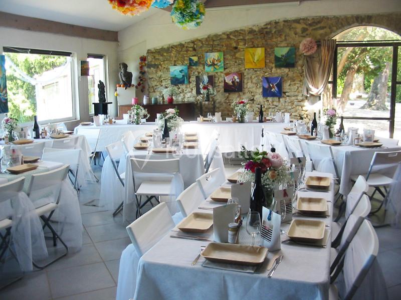 Salle décorée pour un événement, avec des tables dressées, nappes blanches et arrangements floraux colorés.