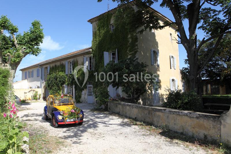Voiture colorée décorée de fleurs garée devant une maison ancienne couverte de lierre, entourée d'arbres.