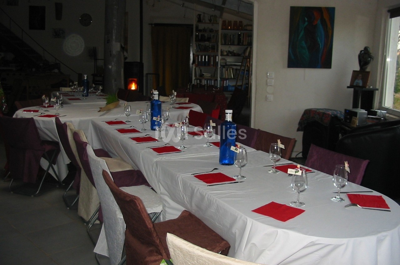 Tables dressées avec nappes blanches, serviettes rouges, verres et bouteilles bleues dans une salle conviviale.