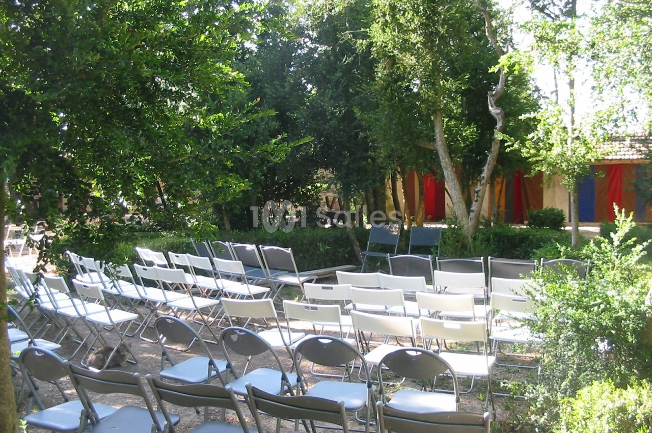 Chaises disposées en rangées dans un jardin ombragé, face à une structure colorée en arrière-plan.