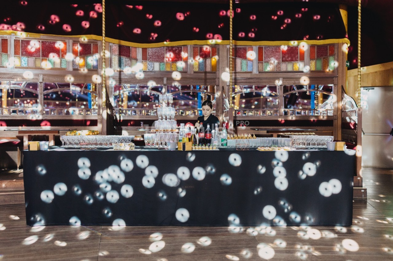 Un bar élégant avec boissons et verres alignés, éclairé par des lumières colorées dans une salle festive.