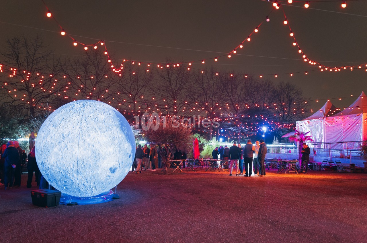 Installation lumineuse représentant une lune géante entourée de guirlandes rouges dans un espace extérieur nocturne.