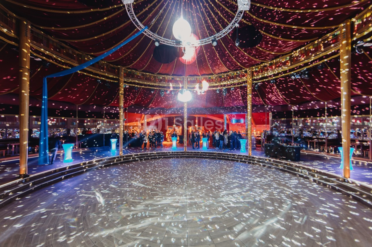 Salle de réception circulaire avec piste de danse éclairée par des lumières scintillantes sous un chapiteau coloré.
