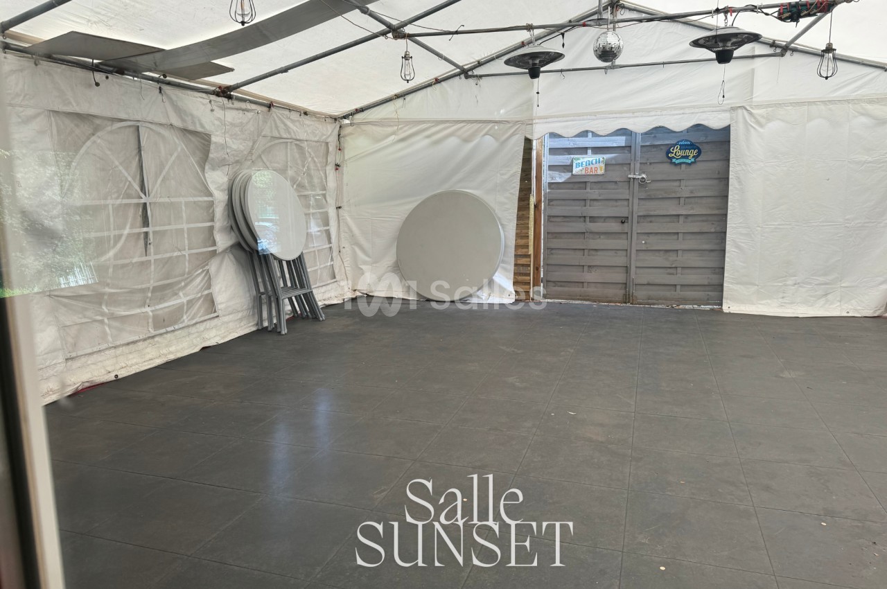 Intérieur d'une tente avec sol en dalles noires, tables rondes pliées et chaises empilées contre un mur.