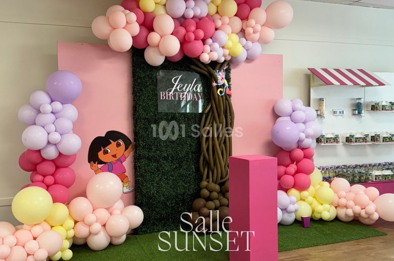 Décoration d'anniversaire avec ballons colorés, fond végétal, et personnages de dessin animé dans une salle festive.