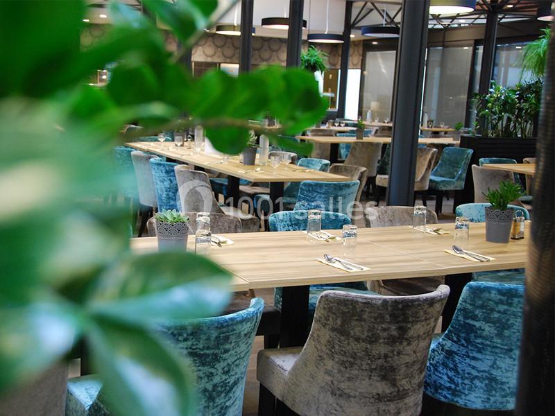 Salle de restaurant lumineuse avec tables en bois, chaises en velours coloré et plantes décoratives.