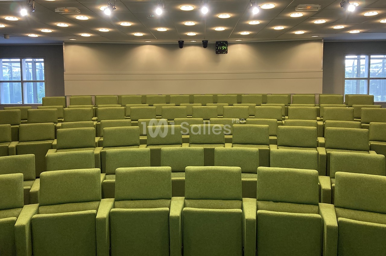 Salle de conférence vide avec des rangées de sièges verts et un plafond éclairé par des spots lumineux.
