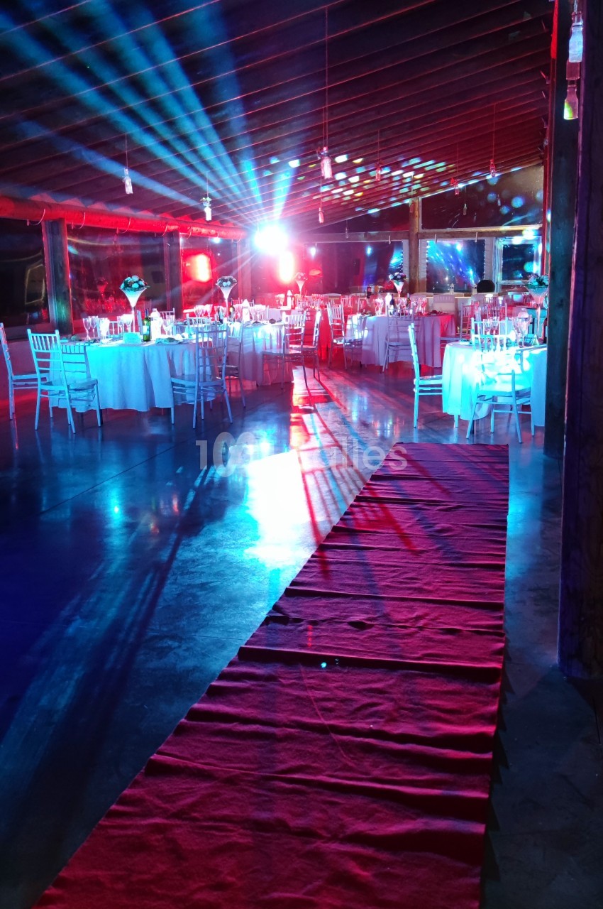 Salle de réception avec tables dressées, éclairages colorés et tapis rouge menant à la scène.