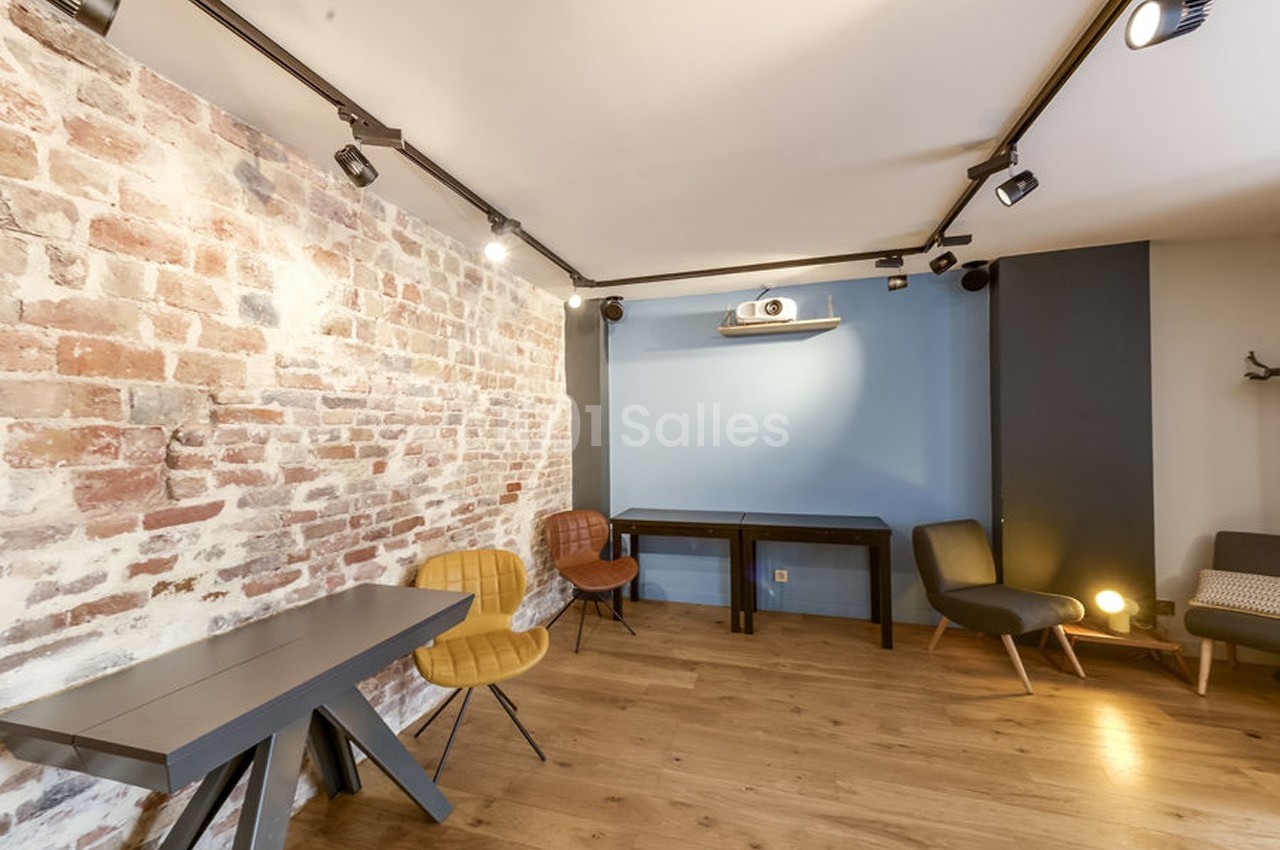 Salle lumineuse avec murs en briques et peinture bleue, parquet en bois, mobilier moderne et projecteur au plafond.