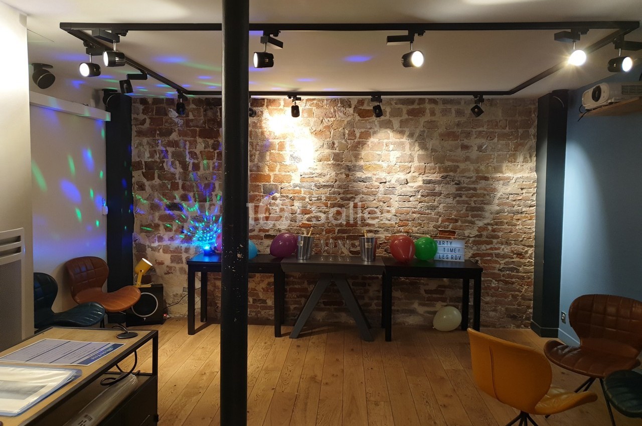 Salle avec mur en briques, parquet, chaises colorées, ballons et éclairage décoratif.