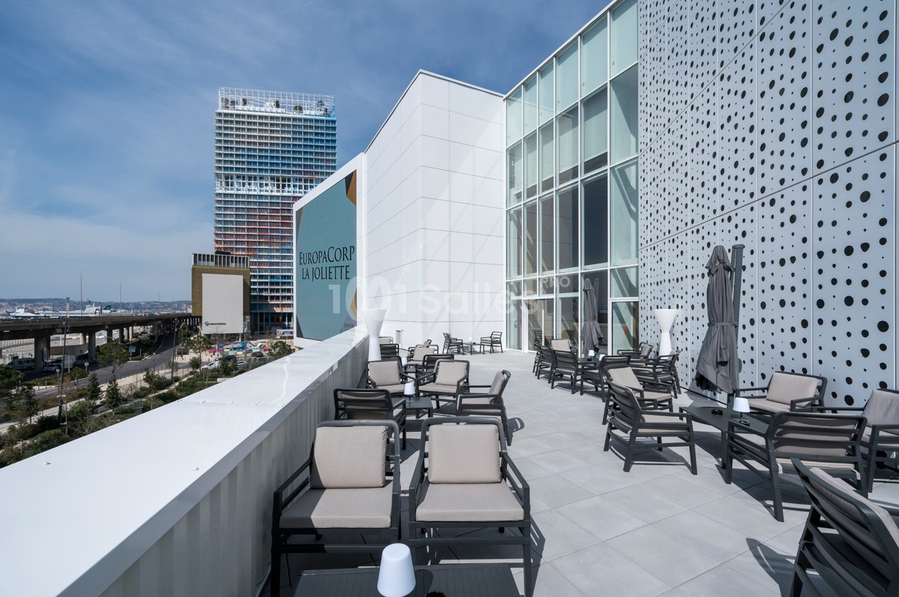 Terrasse extérieure avec mobilier de jardin, vue sur des bâtiments modernes et ciel dégagé en arrière-plan.